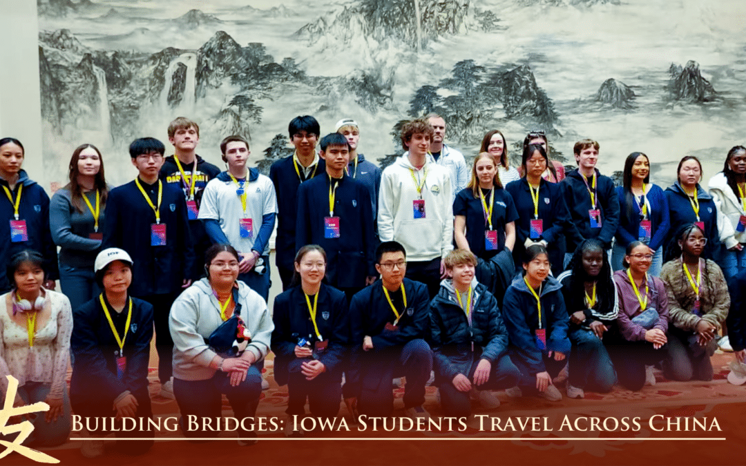 A group of students and adults pose together indoors in front of a large artwork. The caption reads, Building Bridges: Iowa Students Travel Across China.