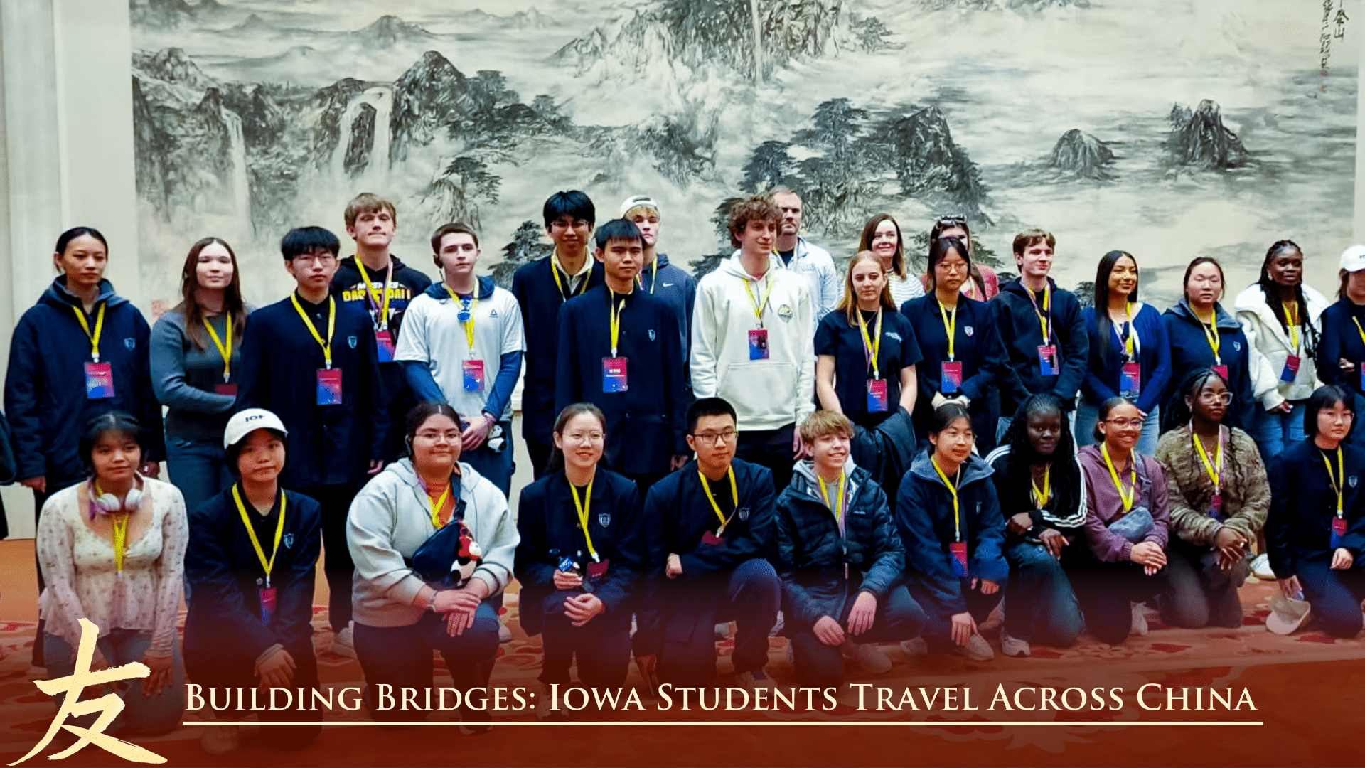 A group of students and adults pose together indoors in front of a large artwork. The caption reads, Building Bridges: Iowa Students Travel Across China.